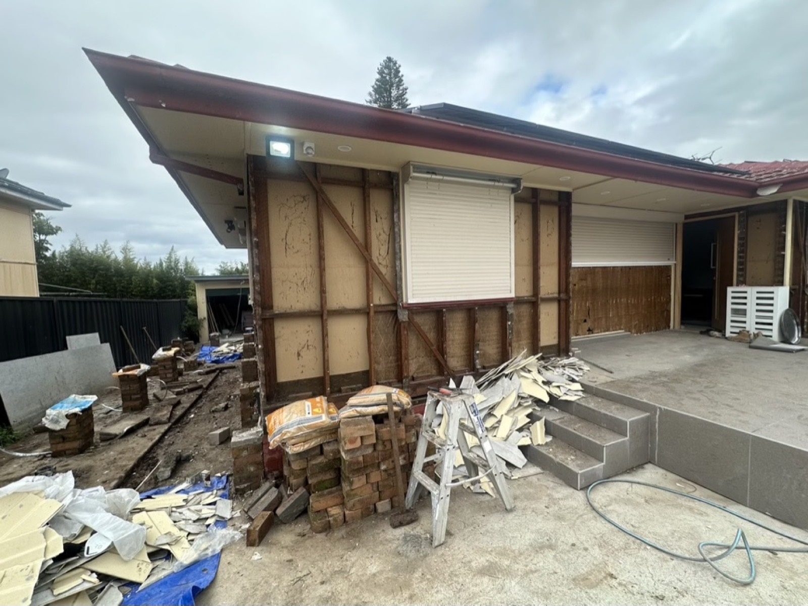 House with cladding stripped, debris and a ladder on site